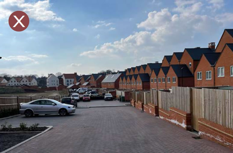 Parking court with limited planting and enclosed by timber fencing.