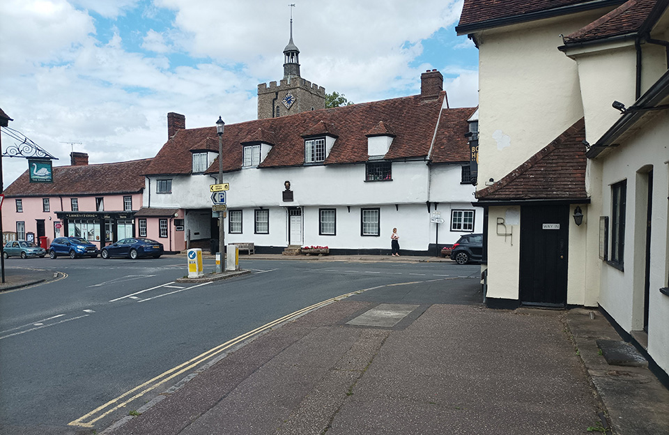 Pedestrians encouraged along wide pavements to the backdrop of historic terraces and Holy Cross Church on Chelmsford Road, Felsted.