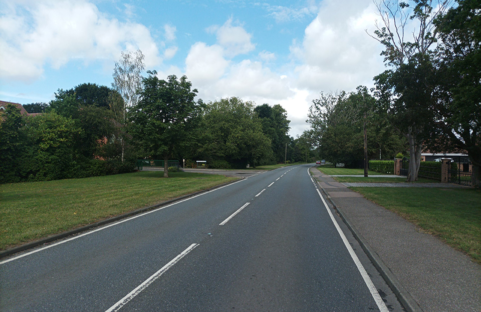 Large trees animate green verges shielding homes from the A1060, Hatfield Heath. Consistent use of white fence posts creates further coherence.