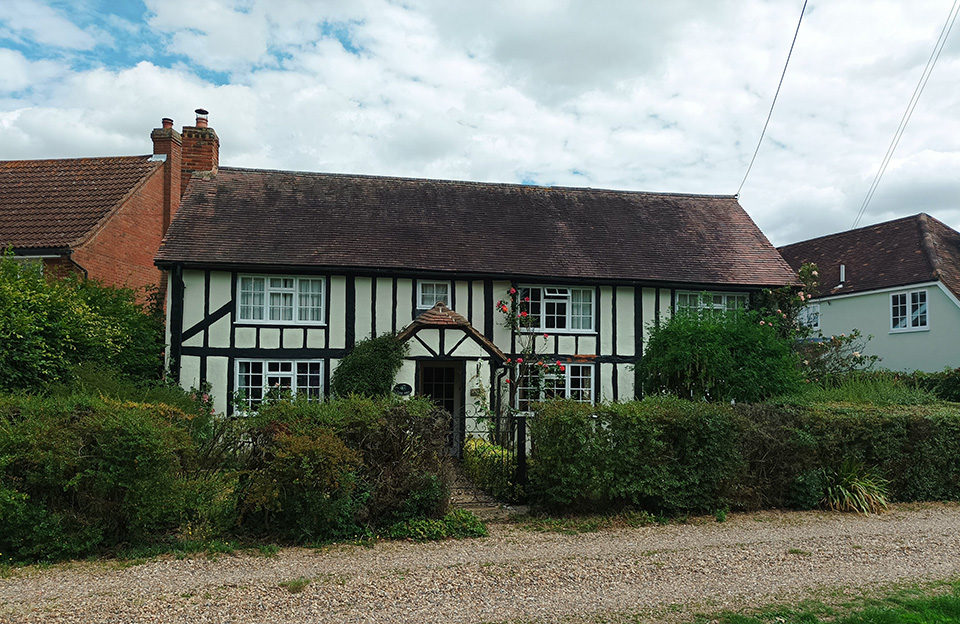 Timber framed cottage with peg tiled roof overlooking Bannister Green. Low hedged boundary treatment integrated with informal shared space.